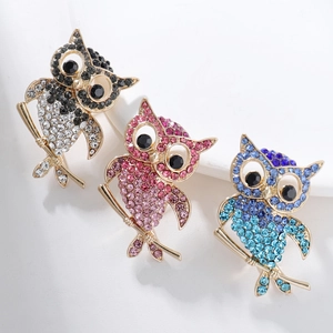 Vue détaillée de trois broches chouettes avec strass colorés sur un fond blanc soyeux