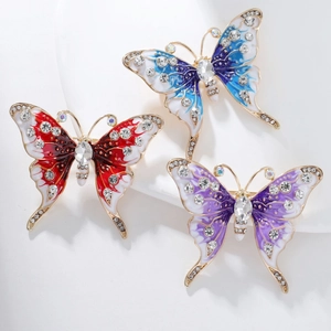 Dettaglio di tre spille a farfalla colorate con strass luminosi e finitura dorata lucida