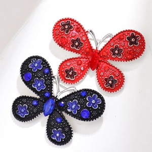 Dettaglio di spille a farfalla vintage con motivi floreali, strass colorati e perle eleganti