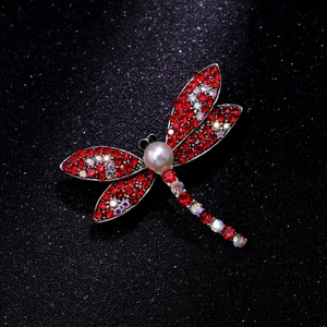 Macro detail of vintage dragonfly brooch featuring red crystals and white faux pearl