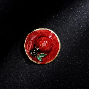 Vintage red wide-brimmed hat brooch with black rose detail on a black matte background