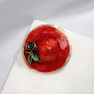 Elegant red sun hat brooch with black rose and golden trim on a textured background