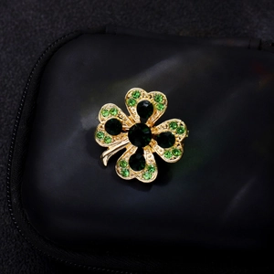 Broche trèfle doré avec zircons verts étincelants sur un support noir élégant