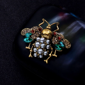 Macro shot of bee brooch with green gemstones and grey pearls on black leather background