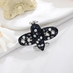 Vintage airplane brooch in dark nickel alloy with blue crystals and pearls on white desk