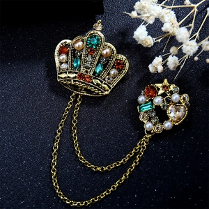 Vintage gold crown brooch with chain tassels and colorful gems on dark background