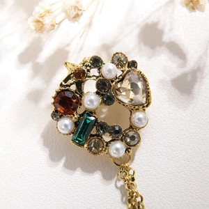 Macro detail of vintage gold brooch with colorful crystals, pearls and metal chain