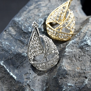 Sparkling silver and gold sailboat brooches with rhinestones on a natural grey rock
