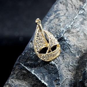 Golden sailboat brooch with sparkling rhinestones on a textured black stone background
