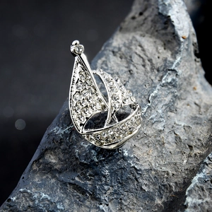 Silver sailboat brooch with pavé-set rhinestones on dark textured stone background