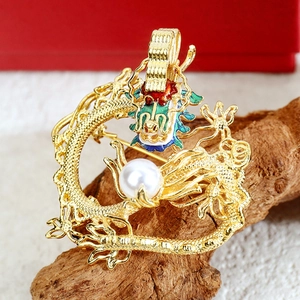 Detailed close-up of a golden dragon brooch with enamel accents and white pearl on wood