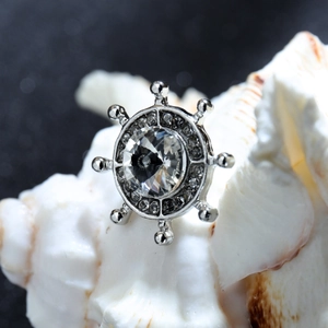 Vue macro d'une broche gouvernail en argent avec cristal posée sur un coquillage blanc