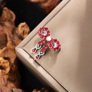 Macro detail of bow brooch featuring red rhinestones and dangling tassel charms