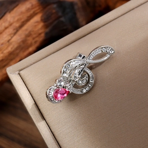 Detail of silver G-clef musical note brooch with white crystals and pink teardrop gem