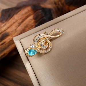 Close-up of golden treble clef brooch with crystals and teardrop blue gemstone