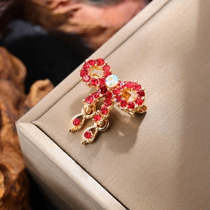 Detailed close-up of a red crystal bow brooch with a gold finish and white opal stone