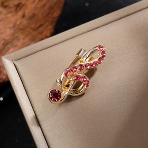 Vue détaillée d'une broche note de musique dorée ornée de strass rose fuchsia