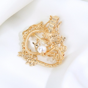 Macro shot of gold dragon brooch with intricate hollow scales and white pearl detail