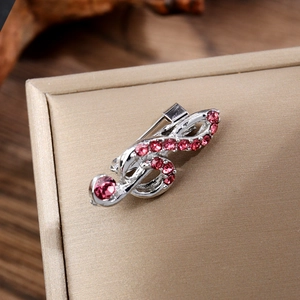 Gros plan de la broche clé de sol argentée avec strass roses sur une boîte à bijoux