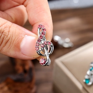 Mini broche clé de sol argentée avec strass roses tenue par les doigts pour la taille