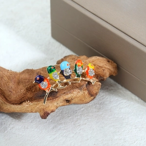Detailansicht von fünf bunten Emaille-Vögeln mit glänzenden Strasssteinen auf Goldzweig