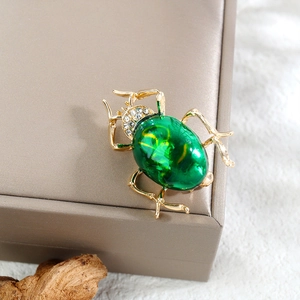 Detailansicht einer Vintage-Käfer-Brosche mit grünen Edelsteinen und goldenen Metallbeinen