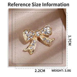 Elegant gold bow brooch with white rhinestones and dimensions shown on silk background