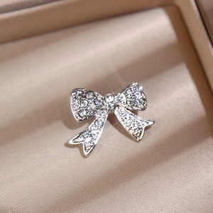 Macro shot of silver bow brooch with sparkling rhinestones on a silk background