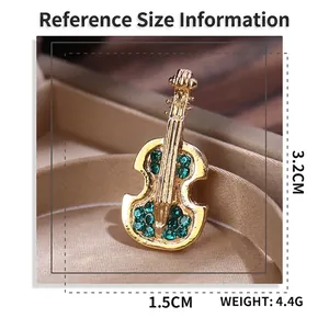 Golden violin brooch with green crystals and size measurements in a luxury setting