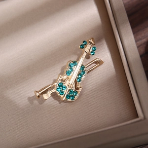 Elegant gold violin brooch with green rhinestones displayed on a velvet jewelry tray