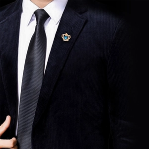 Spilla a corona dorata con gemma a cuore blu indossata su blazer scuro