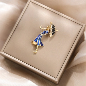Détail d'une broche élégante femme avec robe en émail bleu et parapluie dans un coffret cadeau