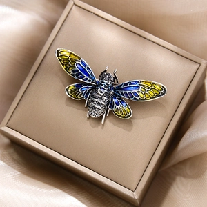 Detailansicht einer Zikaden-Brosche mit blauen Emaille-Flügeln in einer Schmuckschatulle