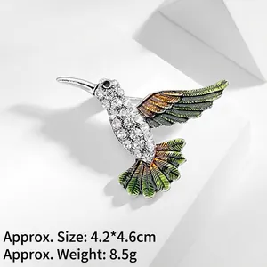Detail of hummingbird brooch featuring pavé crystals and green enamel wings on white decor