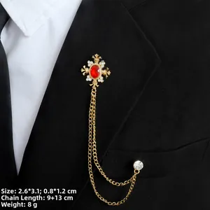 Details einer Kreuzbrosche mit rotem Edelstein und Goldketten am Anzugsrevers