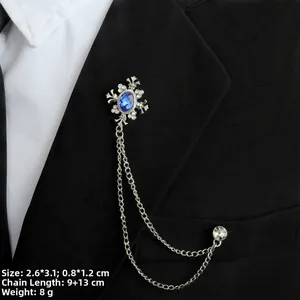 Detail einer silbernen Kreuzbrosche mit blauem Edelstein und Doppelketten am Sakko