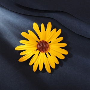 Detailed macro view of vibrant yellow enamel sunflower brooch with textured core on blue fabric