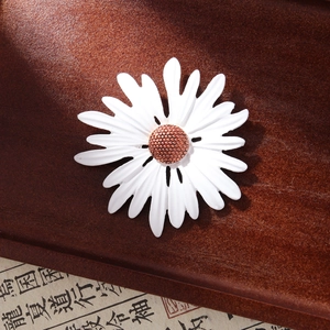 Detailed close-up of white enamel sunflower brooch with textured rose gold core on wood