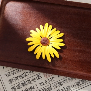 Close-up of yellow sunflower enamel brooch with brown center on vintage paper