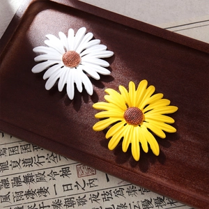 Detailed view of yellow and white enamel sunflower brooches on vintage wooden tray