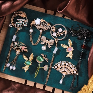 Detailed close-up of hollow fan brooches with tassels and pearls on green velvet tray