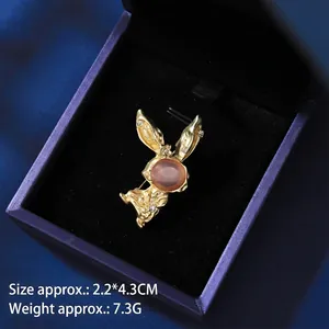 Detailed view of golden rabbit brooch with cat eye stone on dark blue velvet box