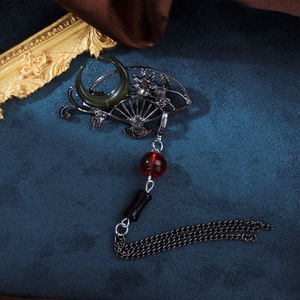 Classic Chinese fan brooch with tassels and red bead on a deep blue textured background