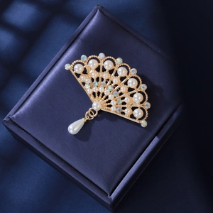 Elegant gold fan brooch with pearls and tassel displayed in a luxury jewelry box
