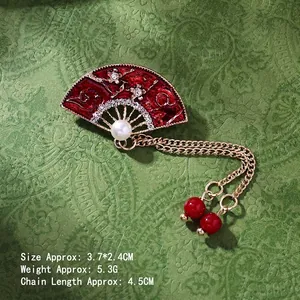 Detail view of fan-shaped brooch with red enamel, white rhinestones and gold tassel chain