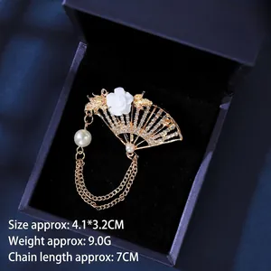 Detailed view of a fan-shaped gold brooch with white rose, tassels and pearls on blue velvet