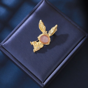 Détail d'une broche lapin dorée sertie d'opale et de cristaux sur un écrin en velours bleu