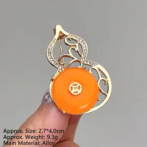 Detailed macro of gold hollow gourd brooch with orange stone and white crystal accents