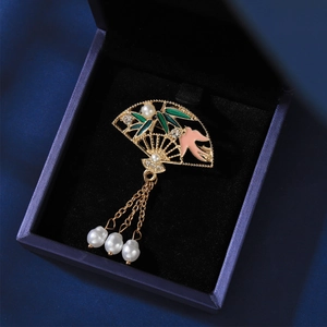 Detailed close-up of hollow gold fan brooch with green bamboo leaf and pink bird detail