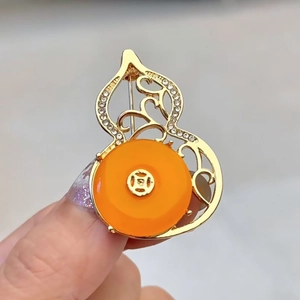 Detailed macro of golden hollow gourd brooch with orange stone and rhinestones